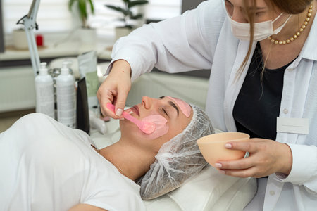 Beautiful woman enjoying rejuvenated pink clay face mask at spa salon. Beauty conceptの写真素材