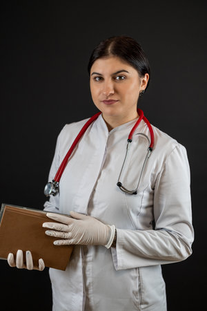 Portrait pretty caucasian nurse wearing uniform with stethoscope holding clipboard isolated on black. Medical staffの写真素材