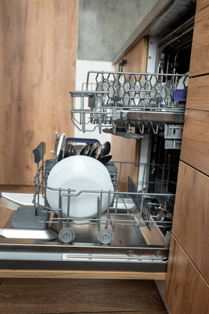 Open integrated dishwasher machine with clean cutlery glasses, dishes. Built-in dishwasher in modern kitchenの写真素材