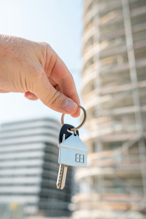 A confident individual proudly displays a key featuring a delightful keychain while standing in front of a building that is presently under constructionの写真素材