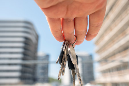 female real estate worker hold keys to apartment on background of multi-storey building. Purchase conceptの写真素材