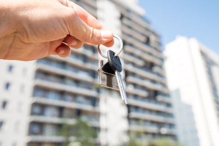 Female hand of realtor holding a set of keys outside, against new building. Buy or rent conceptの写真素材