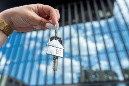 Woman hand holding new house key against the backdrop of urban development, new modern building. Real estate conceptの写真素材