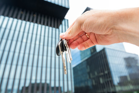 Real estate agent holding house keys outdoors, against new modern glass buildingの写真素材