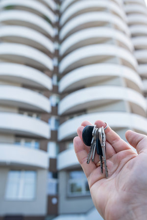 Female hand of realtor holding a set of keys outside, against new building. Buy or rent conceptの写真素材