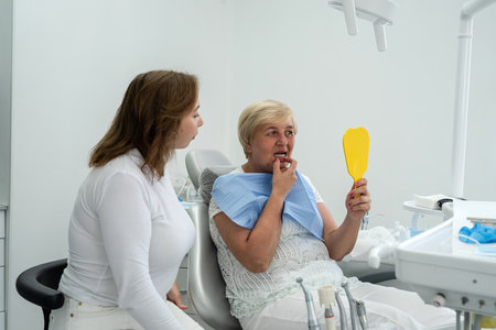 female dentist with elderly woman looking together to the mirror in the dental office. Healthy lifestyleの写真素材