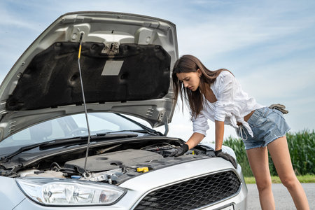 woman driver looking under bonnet of car, broken auto during trip. Engine compartment of a broken down carの写真素材