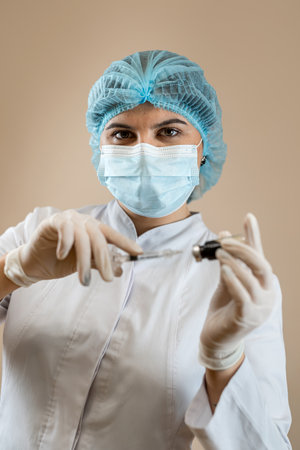 woman doc dressed white coat mask cap and gloves holding syringe with vaccine isolated. Studio shotの写真素材