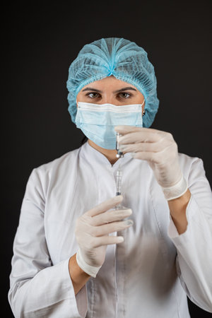 caucasian female doctor in a medical uniform and protective mask and hold syringe with vaccine.の写真素材