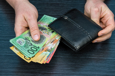 Male hand taking new 50 100 Australian banknotes in black leather wallet. Saving