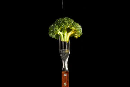 broccoli held by fork on black backgroundの写真素材