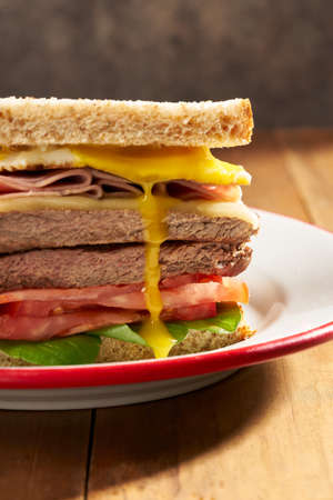 sandwich of meat, vegetables, ham, cheese and broken egg spilling the juice of the yolkの写真素材