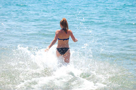 Girl in a swimsuit runs into the sea with sprayの写真素材