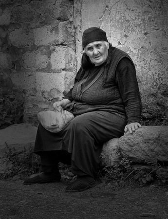 SNO, GEORGIA - JULY 1, 2014: Old woman sitting on a stone in a Caucasian village on July 1, 2014 in Georgia, Europeのeditorial素材