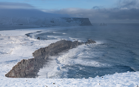 Panoramic image of the coastal landscape of Cape Dyrholaey on a winter day with snow-covered coastline, Icelandの写真素材