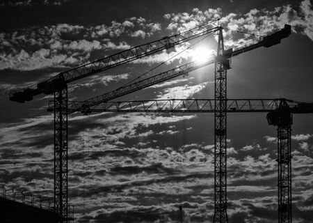 Cranes on a construction site with a cloudy sky during sundownの写真素材