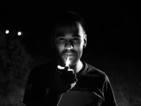 man lighting cigarette outdoors at nightの写真素材