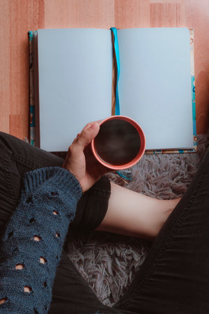 libreta o libro en blanco y una taza de cafÃ© caliente, el personaje solo se ven las manos...