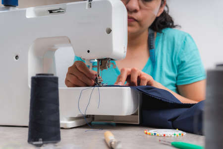 Cheerful woman sewing while sitting at her working place in fashion workshopの写真素材