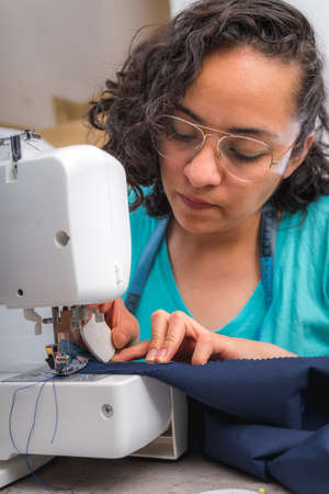 Cheerful woman sewing while sitting at her working place in fashion workshop