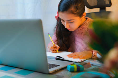 Millennial teenage Caucasian student doing homework at home. Young girl makes notes in front of her...