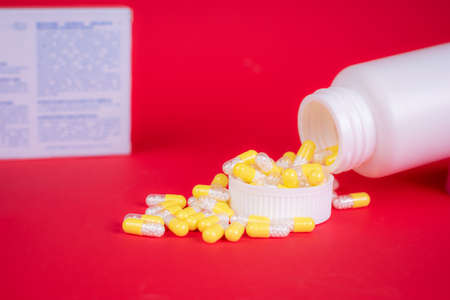 Medicine concept. Yellow capsules scattered from prescription bottle. Background is red color, with space for writing. Studio photo.の写真素材