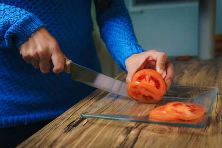 On the table there is a cutting board and you can see a woman's hands cutting white onions with a chef's knife.の写真素材