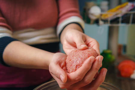 Close-up of a woman's hands preparing ground beef to make hamburgers, the meat is still raw and she is adding the ingredients, nice atmosphere in the kitchen.の写真素材