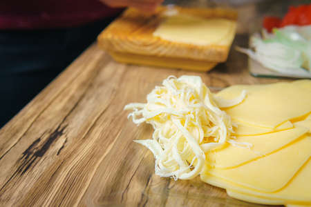 Close-up of a young woman's hands crumbling cheese on a wooden table in a kitchen, preparing a...