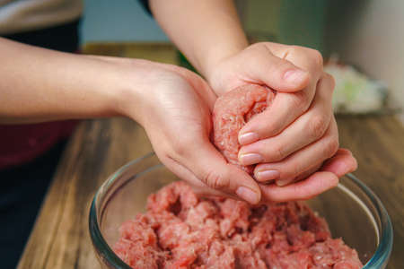 Close-up of a woman's hands preparing ground beef to make hamburgers, the meat is still raw and she is adding the ingredients, nice atmosphere in the kitchen.の写真素材