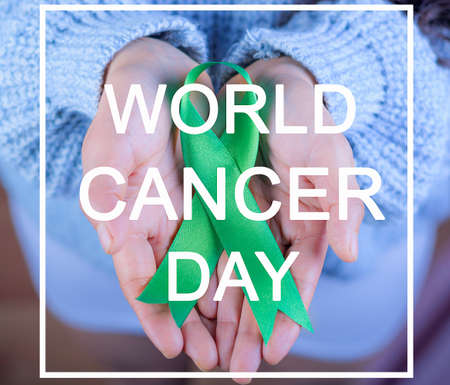 Green ribbon to support liver and adrenal cancer awareness, Human hands holding green ribbon. World Cancer Day. Text with the legend: "world cancer day".の写真素材