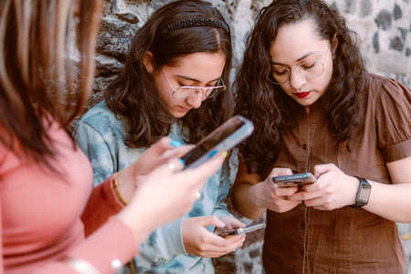 Three beautiful young women walk in the city, using phone outdoorsの写真素材