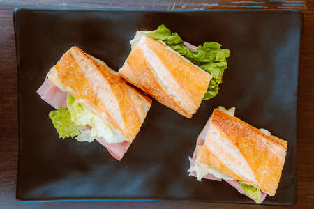 Delicious barbecue chicken sandwich on French bread with tomatoes and lettuce, on a black plate.の写真素材