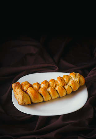 Homemade braided bread filled with strawberry jam on a white plate with rustic black background,...