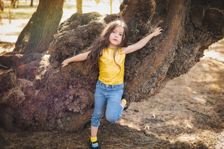 A girl in the forest is posing in a tree, she is wearing a yellow blouse and denim pants with a children's day theme.の写真素材