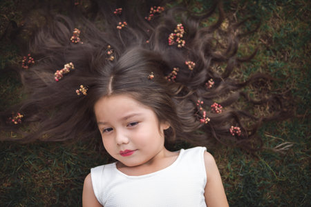 Little girl in white dress lying on the grass, she is smiling and her hair is very long and princess-like, children's day theme.の写真素材