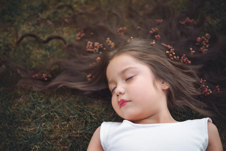 Little girl in white dress lying on the grass, she is sleeping, her hair is very long and princess-like, she plays with her hands on the theme of children's day.の写真素材