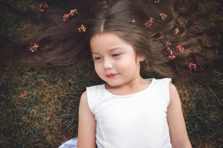 Little girl in white dress lying on the grass, she is smiling and her hair is very long and princess-like, children's day theme.の写真素材