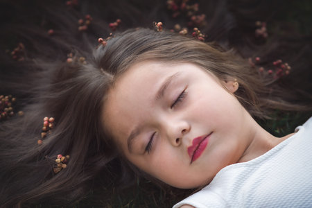 Little girl in white dress lying on the grass, she is sleeping, her hair is very long and princess-like, she plays with her hands on the theme of children's day.の写真素材