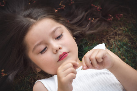 Little girl in white dress lying on the grass, she is sleeping, her hair is very long and princess-like, she plays with her hands on the theme of children's day.の写真素材