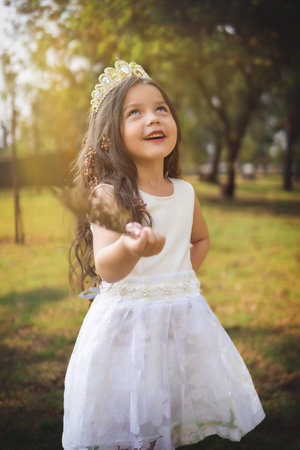 Little girl in white dress and princess crown, she poses for the camera with a beautiful look, copy space, children's day theme.の写真素材