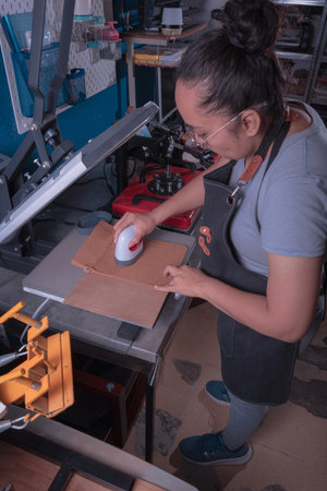 Young working woman in her workshop makes the sublimation process with a label plate, printing and...