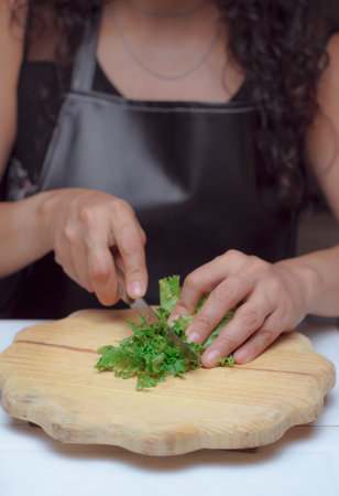 Hands of a cook with a knife cutting fresh lettuce leaves on a wooden board, chef in her kitchen is preparing vegetarian food.の写真素材