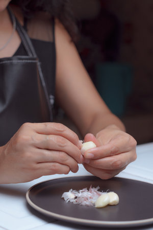 A woman chef in the kitchen is peeling garlic on a plate, preparing ingredients for cooking.の写真素材