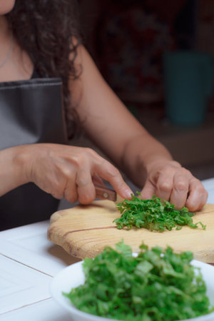 Hands of a cook with a knife cutting fresh lettuce leaves on a wooden board, chef in her kitchen is preparing vegetarian food.の写真素材