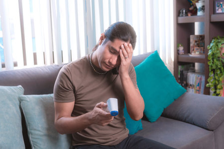 A man measures his temperature with a digital infrared thermometer at home sitting on the couch.