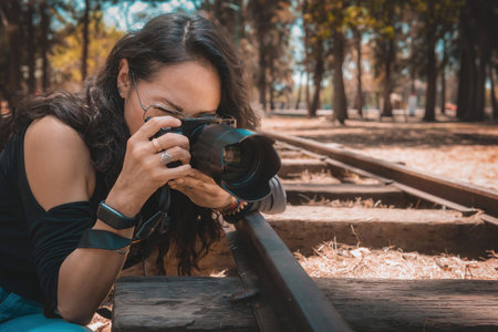 Woman photographer holding a professional camera, is taking a picture in the park focusing on something on the ground.の写真素材