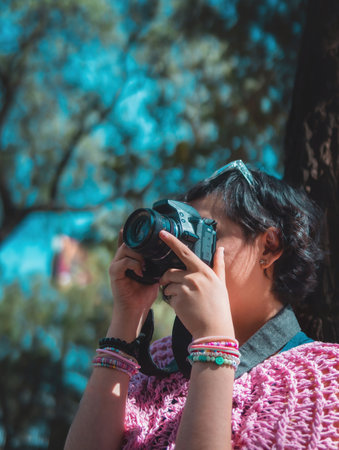Woman photographer holding a professional camera, is taking a picture in the park focusing on something.の写真素材