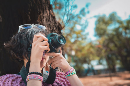 Woman photographer holding a professional camera, is taking a picture in the park focusing on something.の写真素材