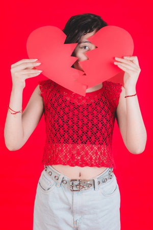 Young girl holds a red paper heart, she makes cheerful expressions, concept of love.